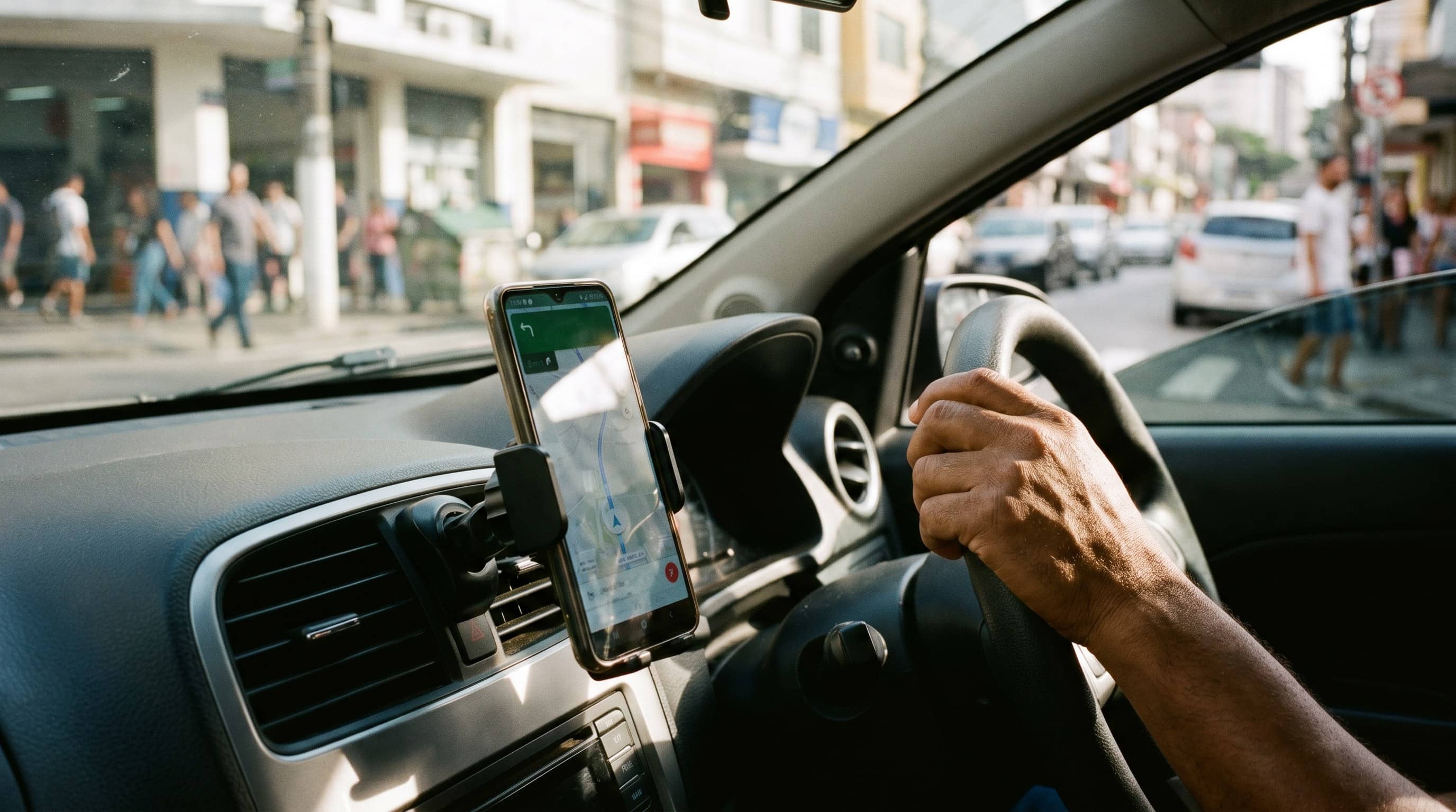 Smartphone em suporte na saída de ar do painel com mão do motorista ao volante em rua urbana