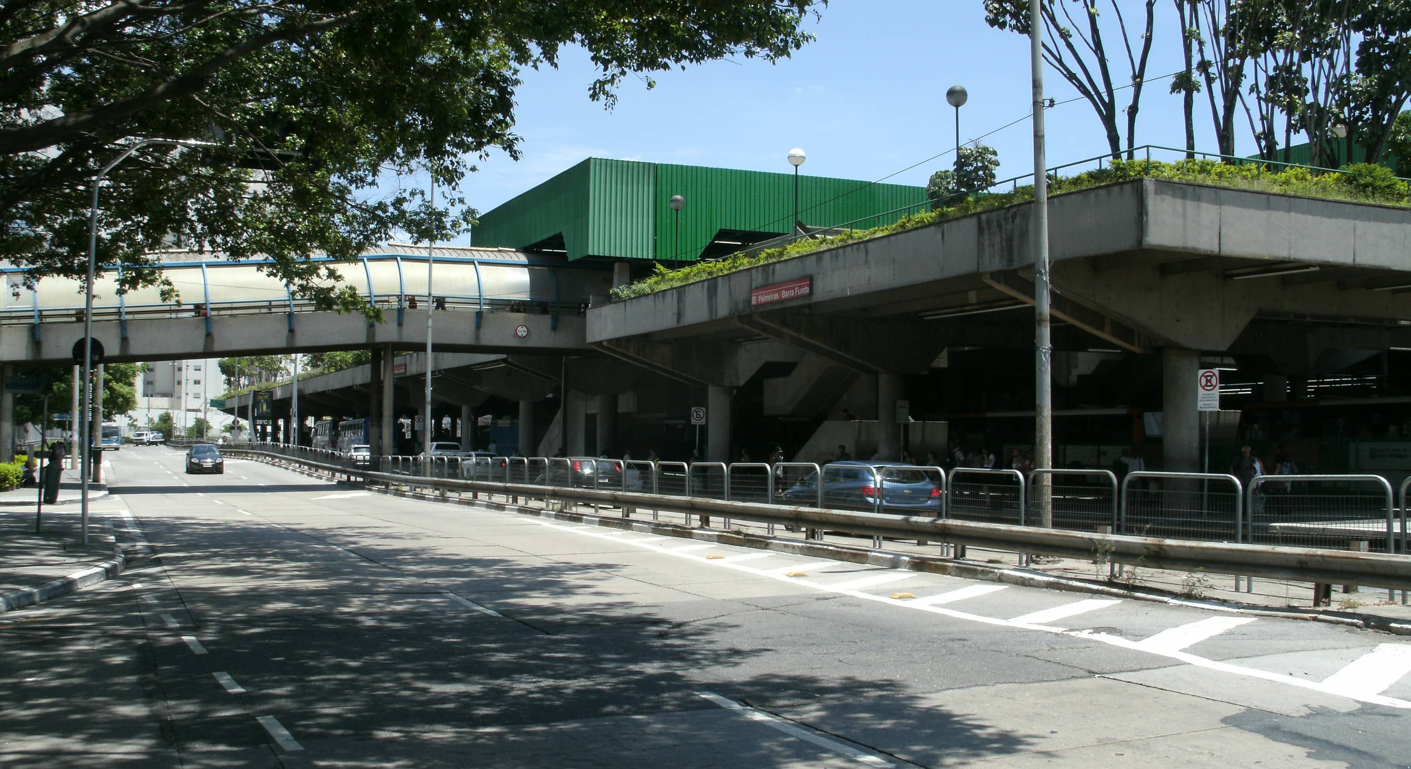 Estação Palmeiras-Barra Funda vista da avenida, com plataforma elevada, passarela e carros passando em dia ensolarado