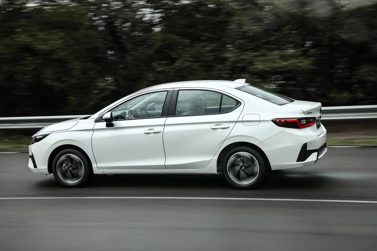 Honda City Sedan 2027 branco visto de lado em movimento em uma via arborizada.