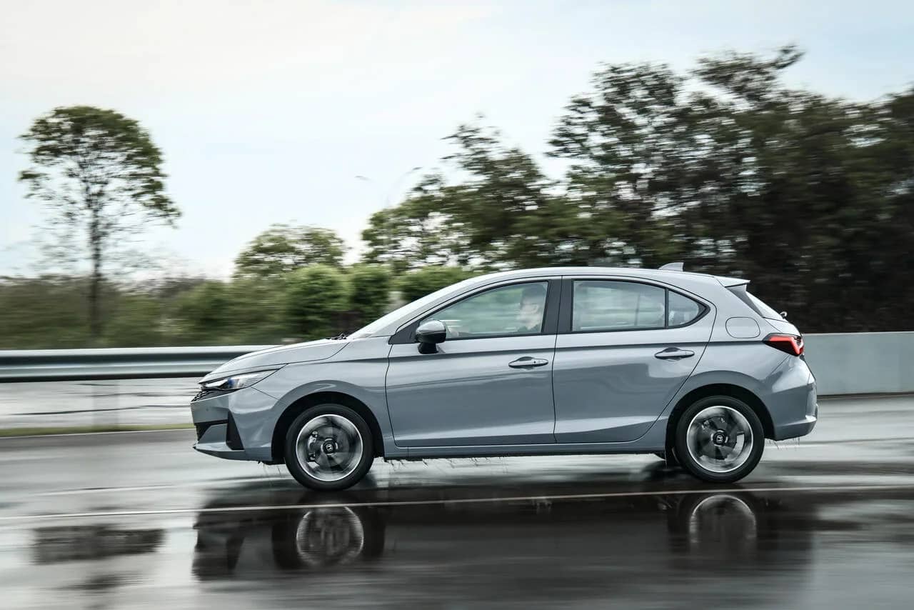 Honda City Hatchback 2027 cinza, visto de lado em uma pista molhada.