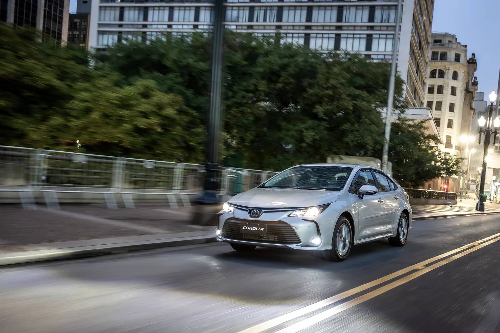 Toyota Corolla 2026 visto de frente e de lado em movimento em uma via urbana.