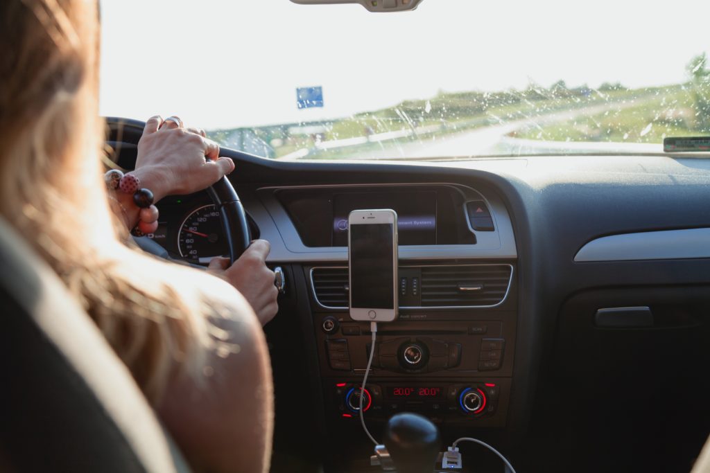 Mulher dirigindo carro na estrada com celular no painel.