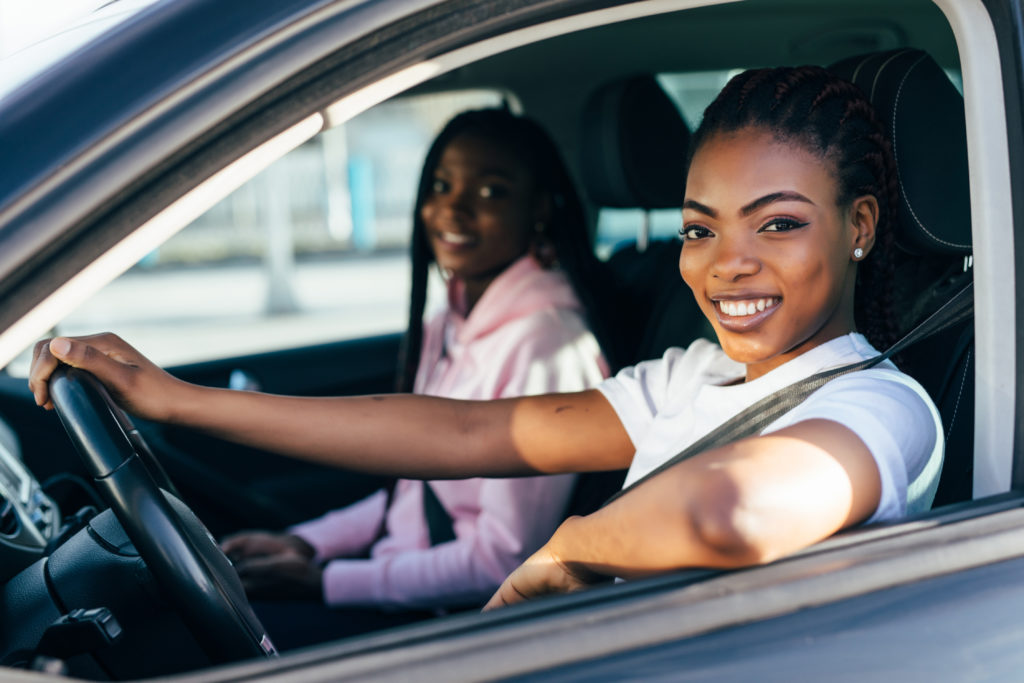 Mulher e menina negras, dentro de carro, sorrindo para a foto.