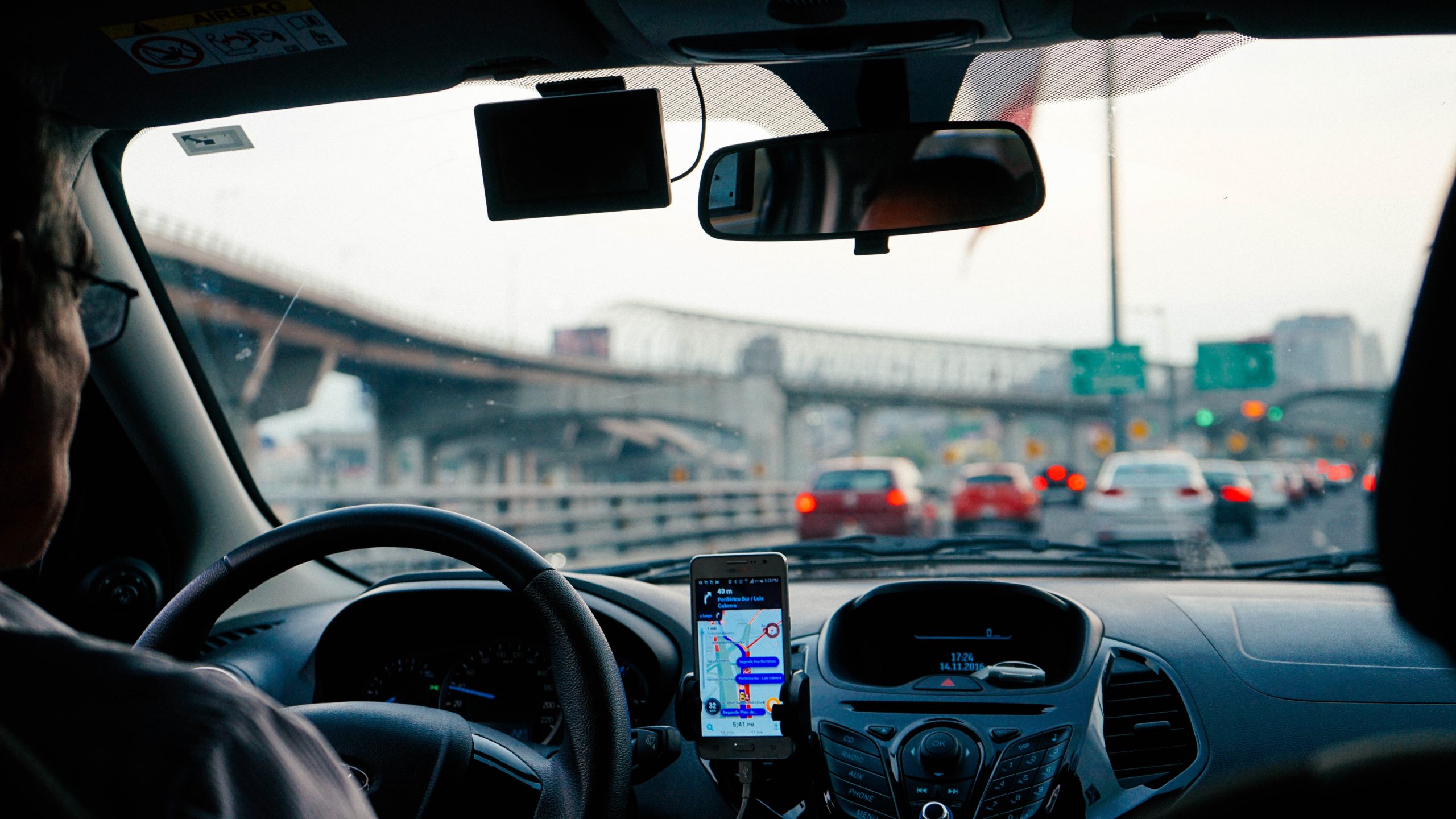 Foto por dentro do carro mostrando painel e telefone em rodovia.