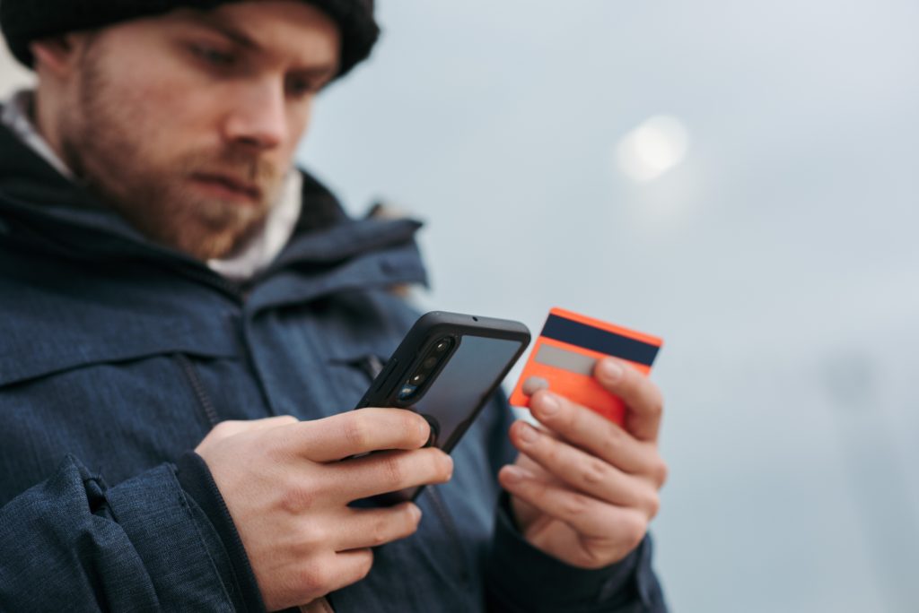 Homem branco vestindo uma jaqueta jeans cadastrando um cartão de crédito no app para controle financeiro no seu celular.