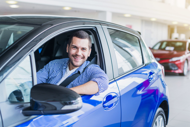 Homem sorridente dentro de um carro azul procurando pelos melhores carros para se comprar