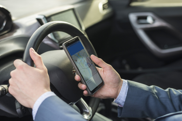Uma pessoa ao volante com um celular em sua mão verificando as principais regras de trânsito