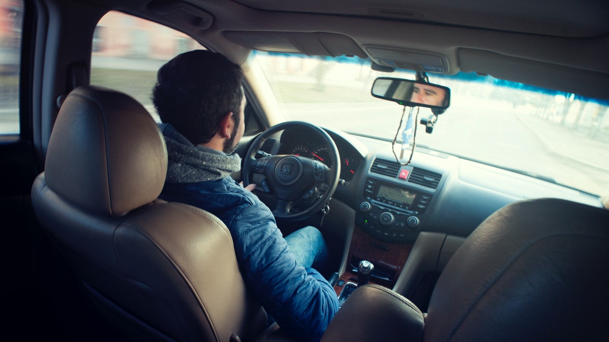 Interior de um carro com um rapaz ao volante dirigindo o carro refletindo sobre as dinâmicas da uber e da 99