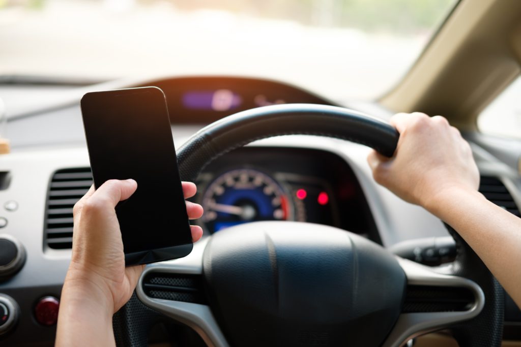 Motorista segurando o volante com uma mão e o celular com a outra.