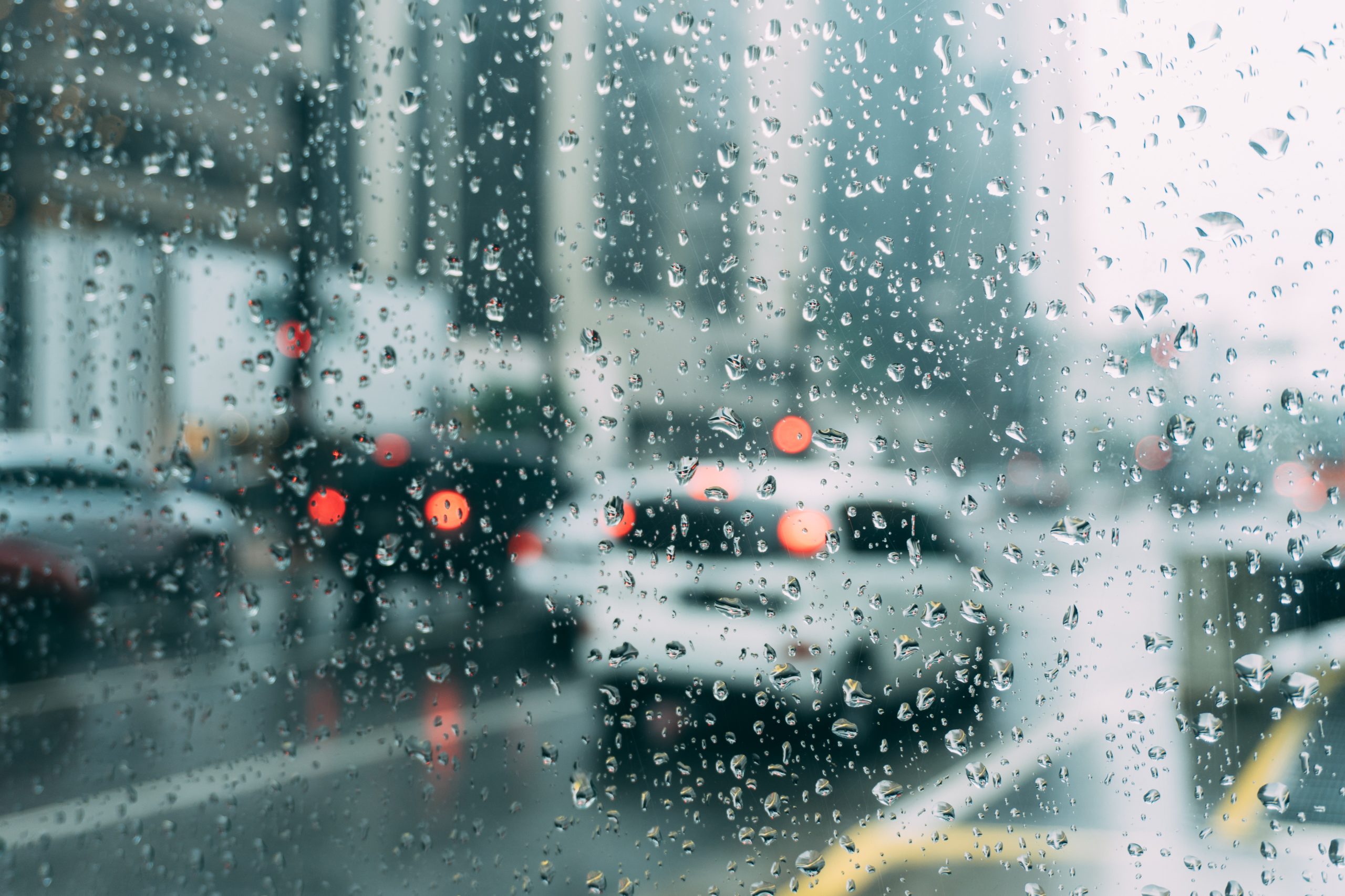 Vidro molhado da chuva enquanto carros andam na rua.