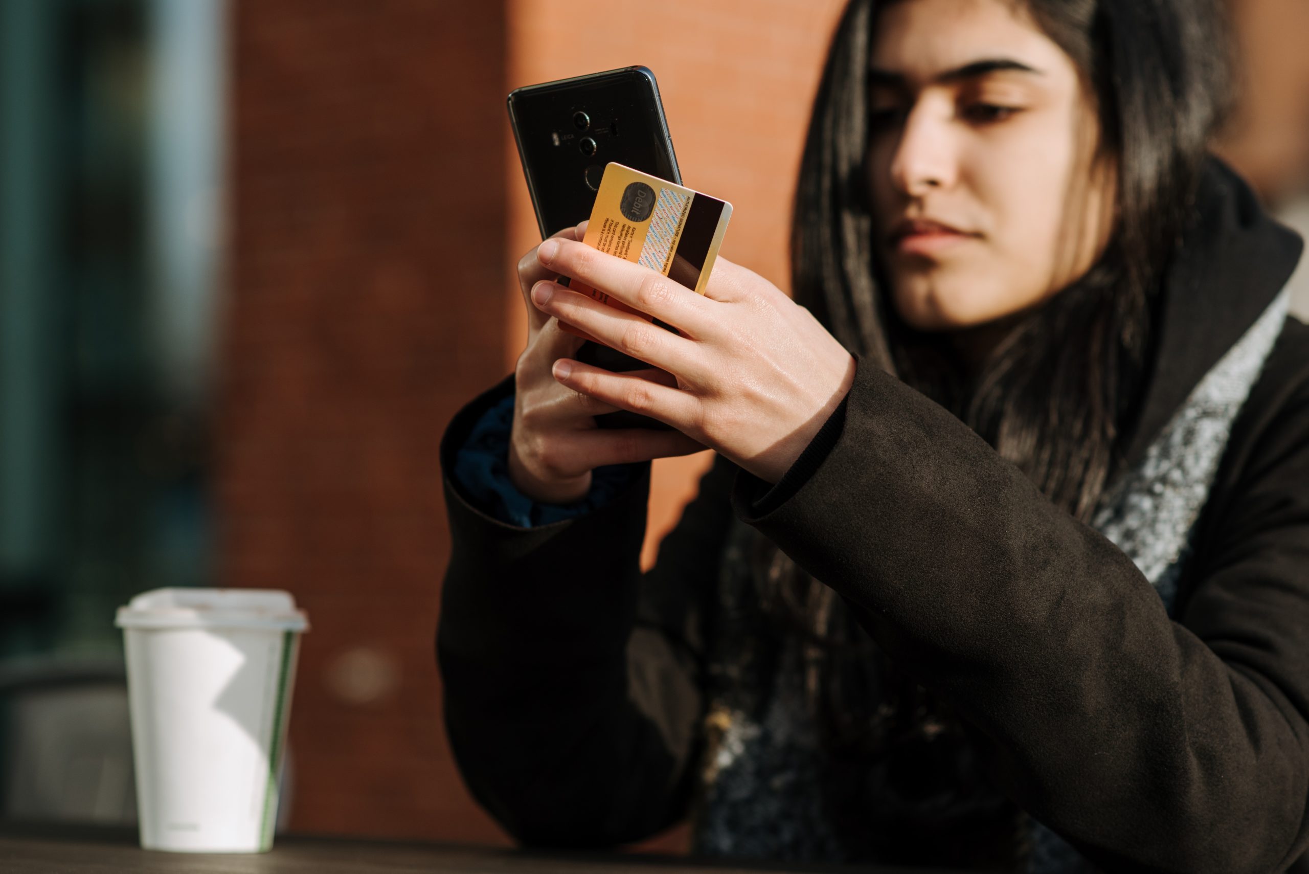 Pessoa mexendo no celular enquanto segura um cartão de crédito.
