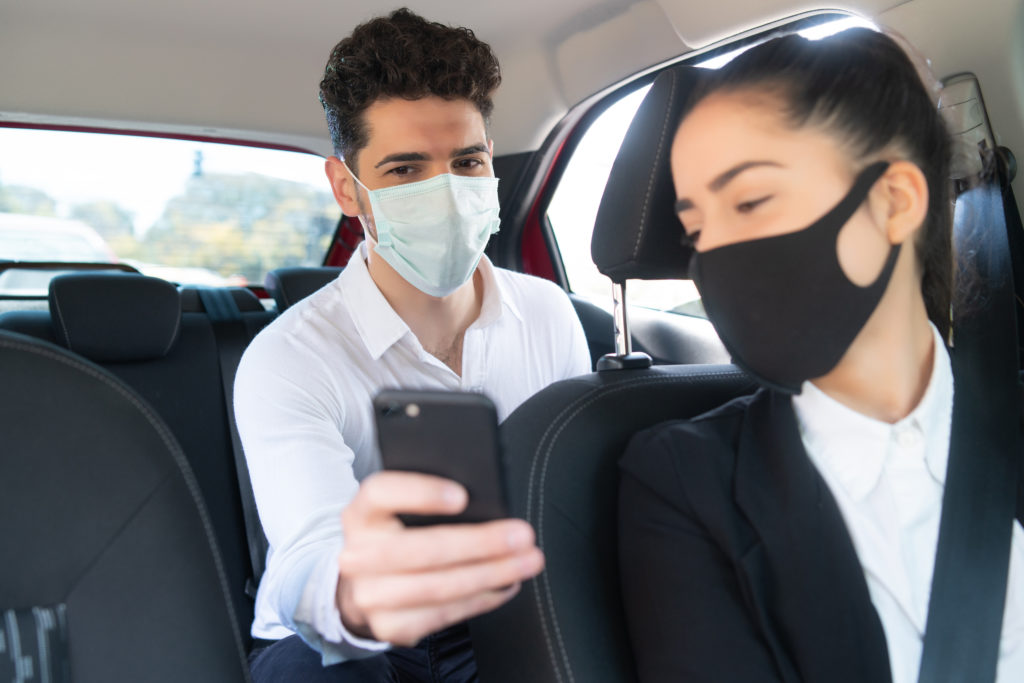 Passageiro mostrando a tela de seu celular para motorista do veículo. Ambos usando máscara.