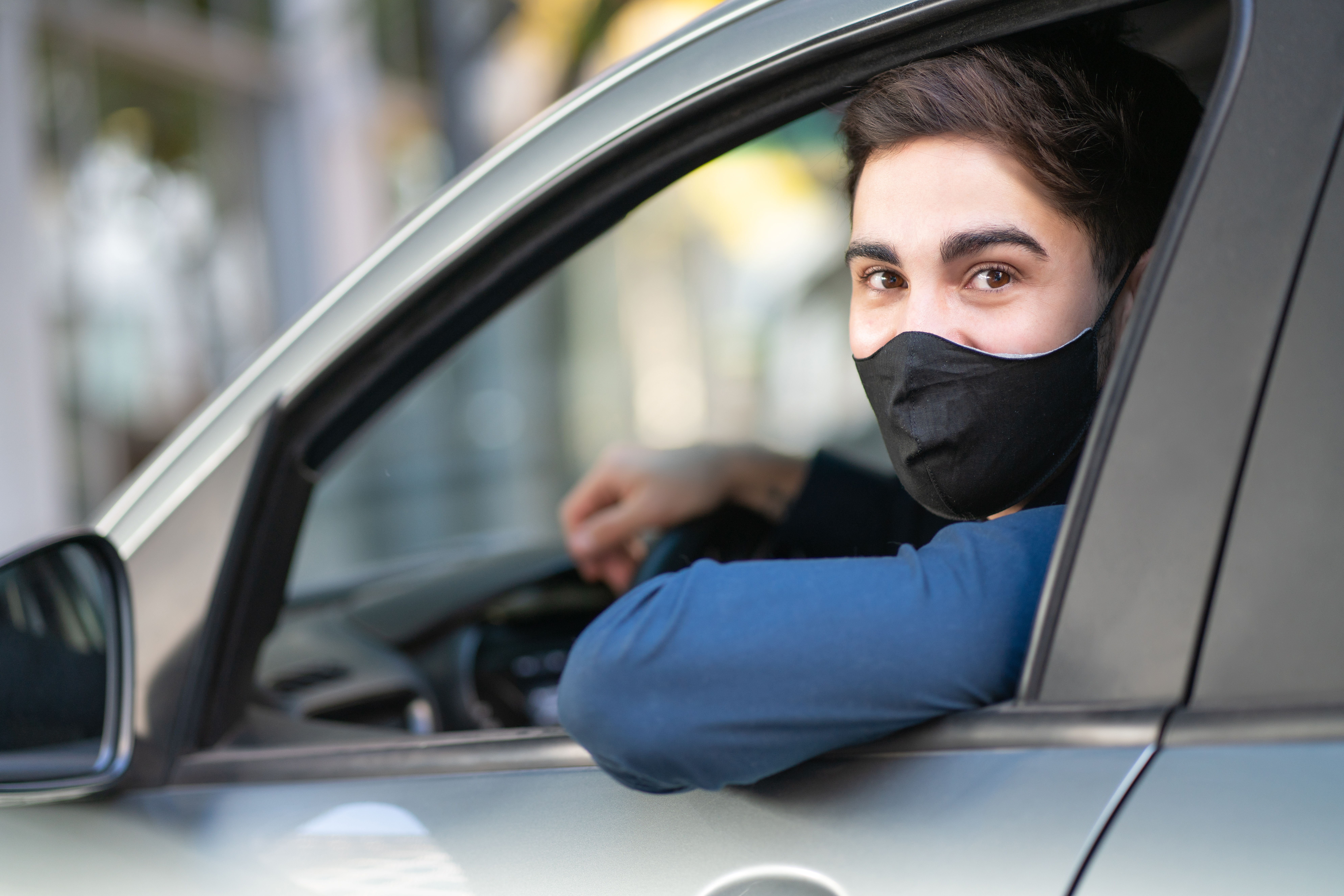Motorista usando máscara e olhando para fora do carro pela janela.