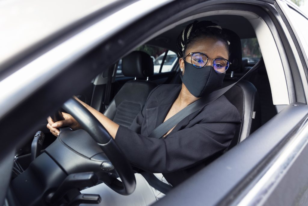 Motorista dirigindo usando máscara, olhando no retrovisor.