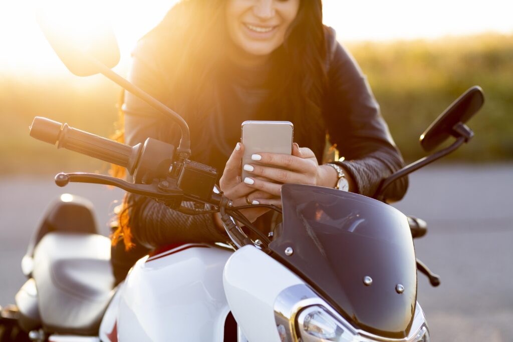 Mulher em cima de moto olhando o celular.