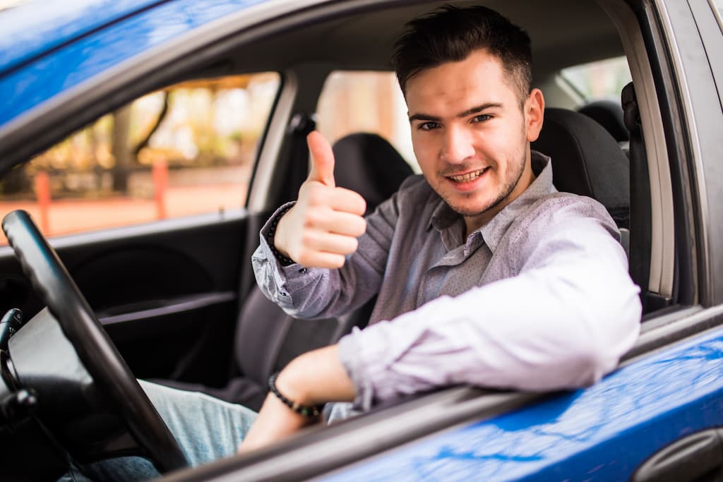 Homem fazendo sinal de positivo dentro de um carro azul.