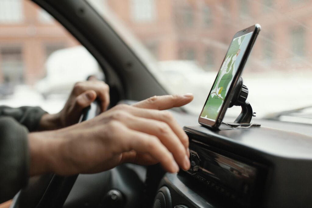 Mãos do motorista em movimento para clicar na tela do celular posicionado no painel do veículo.