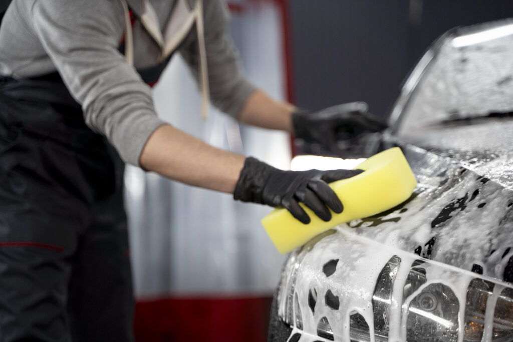 Pessoa utilizando uma esponja para lavar a superfície de um carro cheio de espuma.