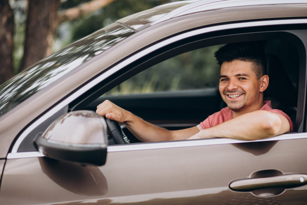 Motorista sorrindo e olhando para fora com o braço apoiado na janela do carro.