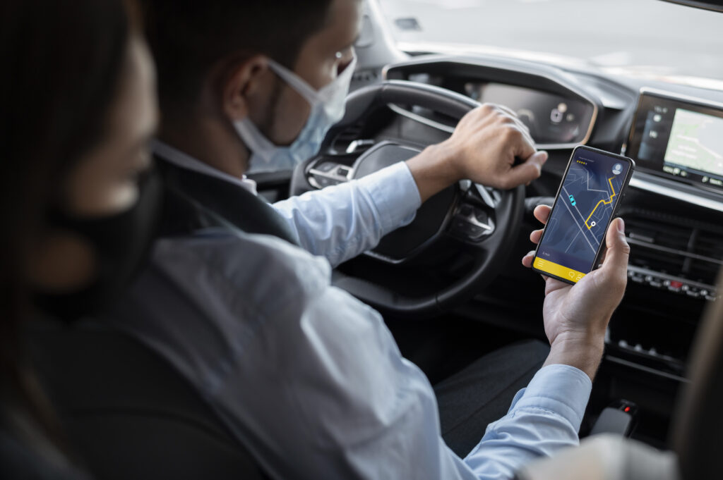 Motorista usando máscara e vestindo camisa azul conferindo localização no GPS do celular.