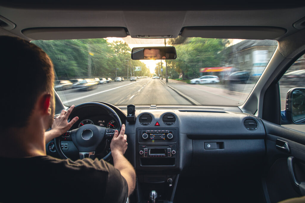 Imagem feita do banco de trás, mostra um homem dirigindo um carro.