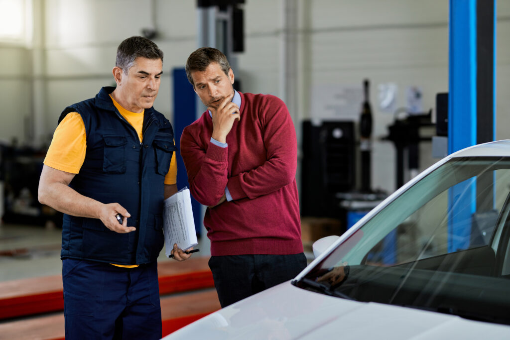 Mecânico e cliente observando carro após o conserto.