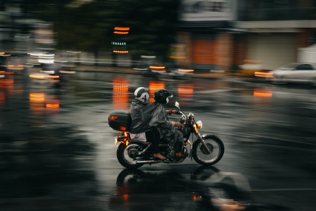 Motociclista, com passageiro na garupa, dirigindo na chuva.