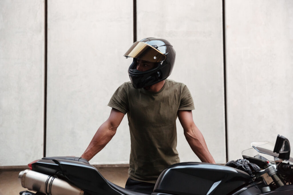 Motociclista, utilizando capacete, apoiado lateralmente em sua moto.