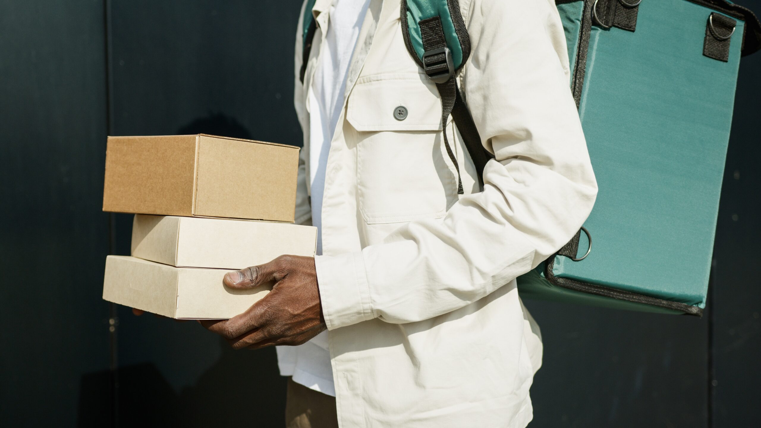 Entregador carregando diferentes pacotes, utilizando bolsa de entrega nas costas.