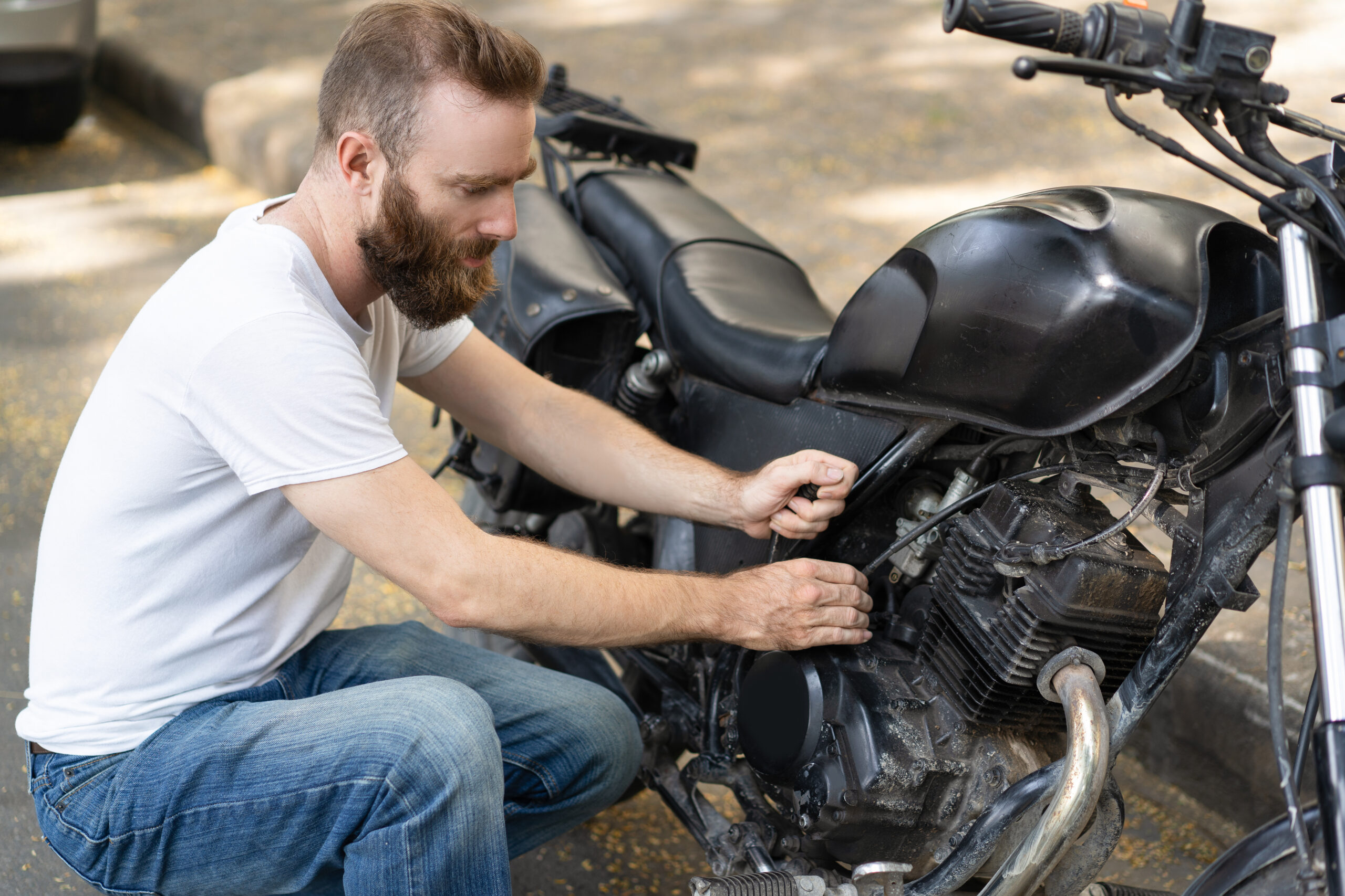 Homem agachado ao lado de uma moto preta, com as mãos em seu motor.