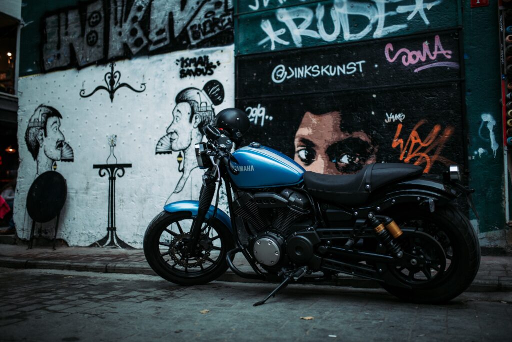 Moto Yamaha azul estacionada, vista de lado. Ao fundo, muros com grafites.